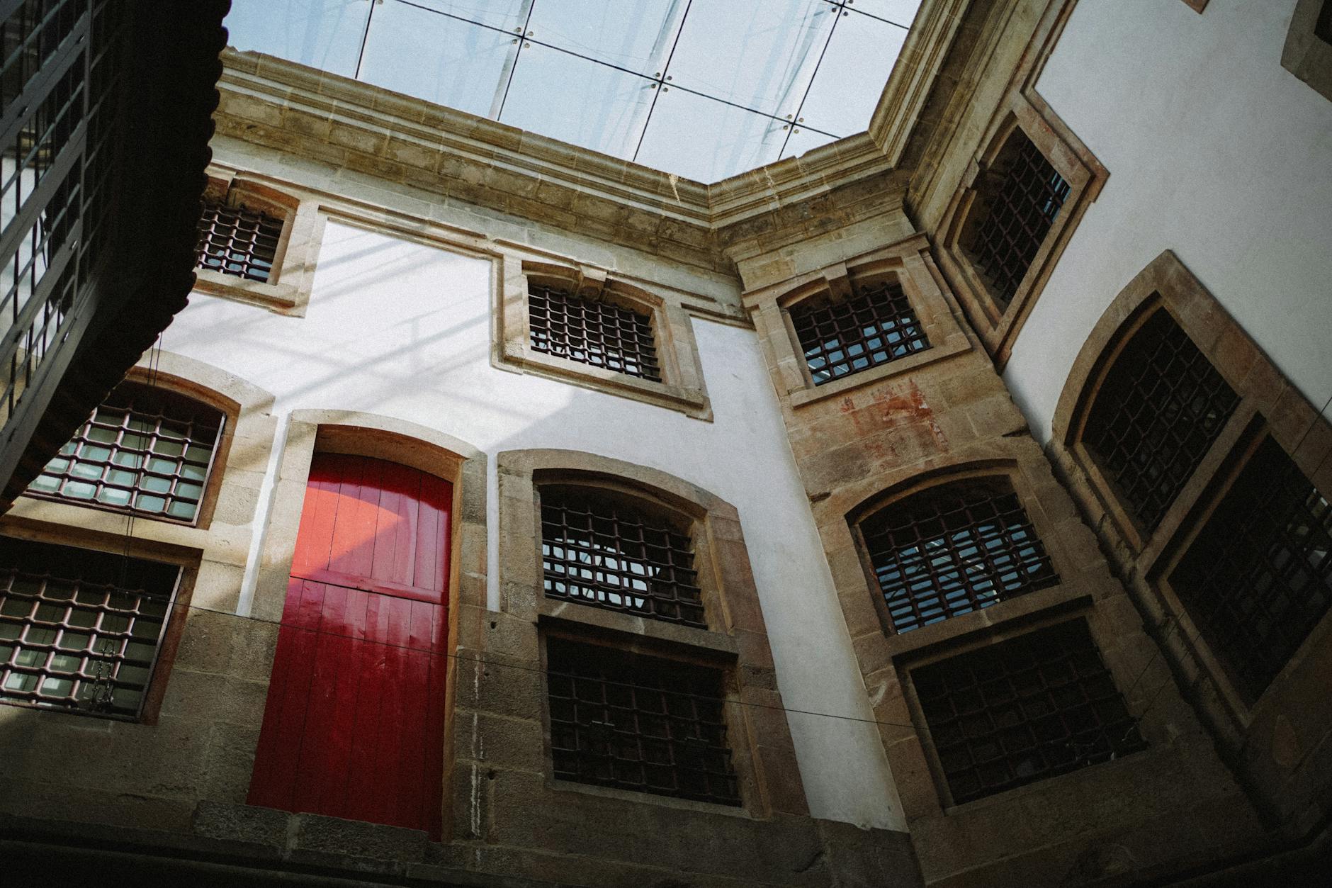 Intriguing view of a historic building's interior with a striking red door and grid windows in Porto, Portugal.